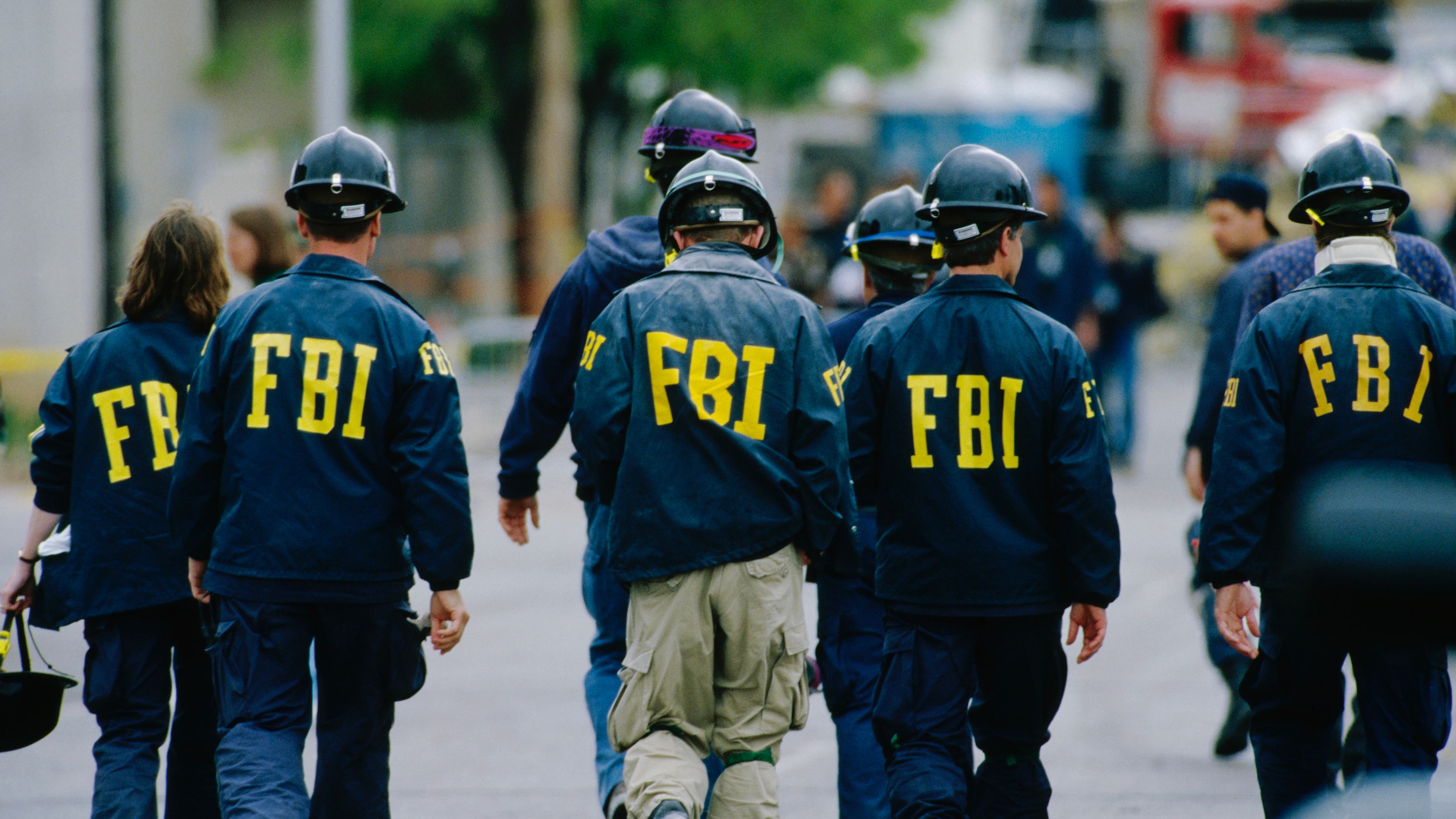 Five agents wearing hard helmets and FBI windbreakers, seen from the back.