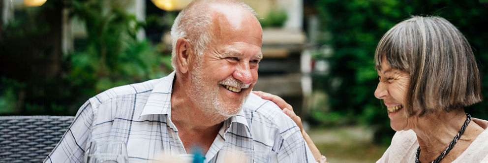 An older man and woman share a laugh together in a sunny backyard.