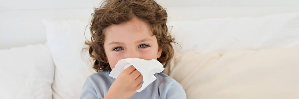 A young boy blows his nose with a tissue.