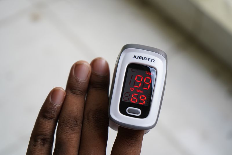 close up of a pulse oximeter clipped onto the finger of a person with a darker skin tone