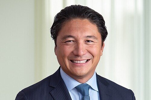 Headshot of smiling man of Asian descent with slicked back dark hair wearing a suit and tie