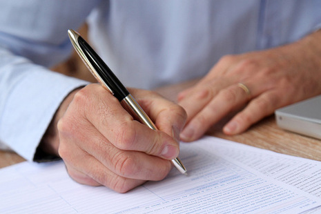 Image of a hand and a pen filing in a form - image licenced by ingram image