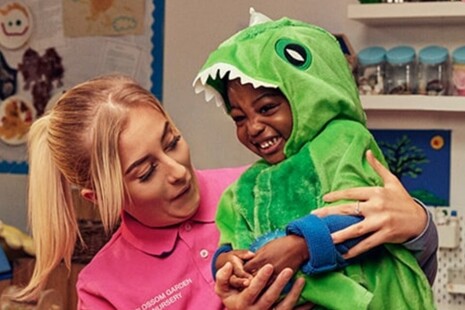 early years teacher holding a toddler wearing a dinosaur outfit