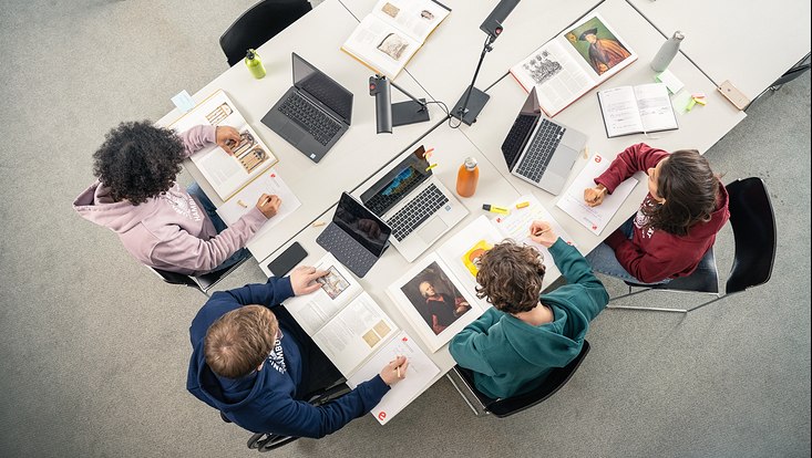 Personen sitzen mit Laptops und Büchern an einem Tisch.