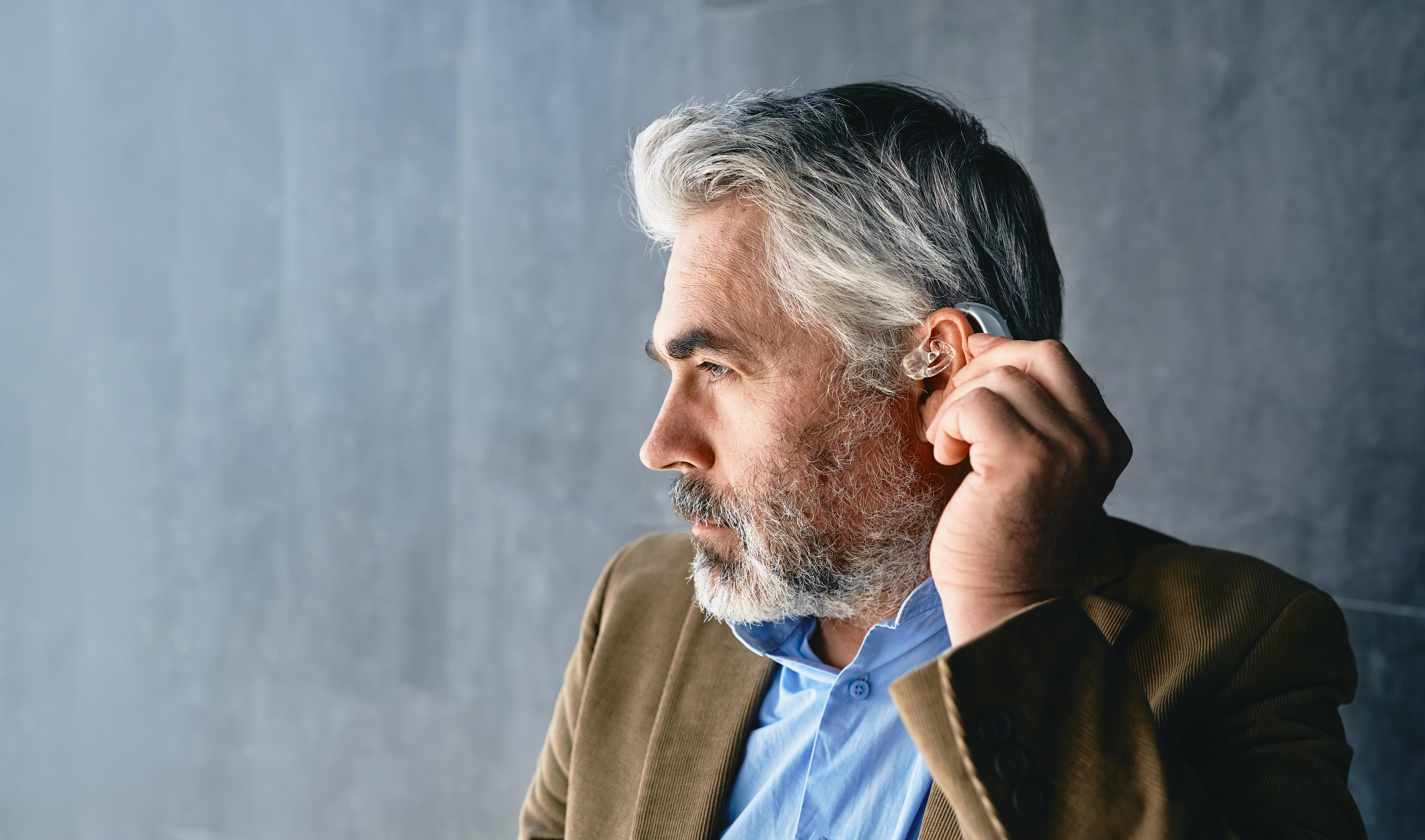 Grey-haired mature man with hearing impairment using hearing aid. Hearing solutions for deafness people 