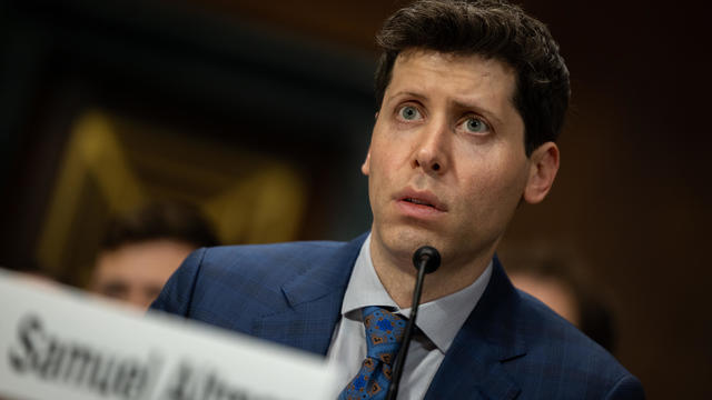 Sam Altman behind a mic in blue suit 