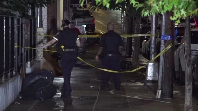 Two police officers string up crime scene tape on a sidewalk in the Bronx. 