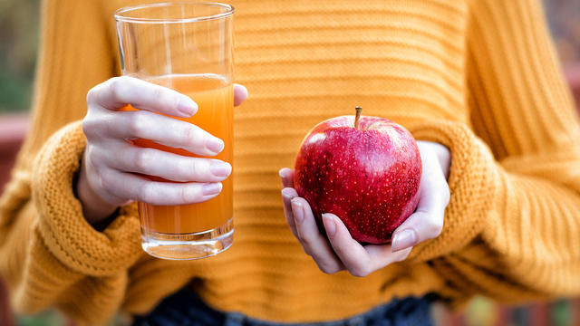 Young woman holding glass of apple juice and fresh apple 