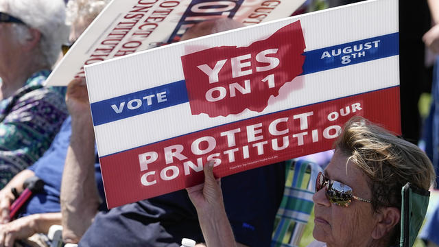 An attendee uses a sign to shield the sun during a rally on Sunday, Aug. 6, 2023, in Norwood, Ohio. 