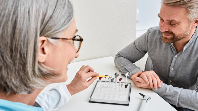 Female audiologist offers BTE hearing aids to man patient with hearing problems for treatment his deafness. Hearing aid selection 