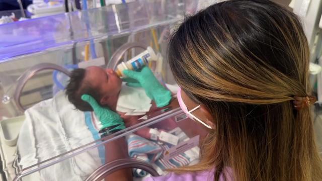 Flushing Hospital NICU nurse Christine Parasram feeds a baby in an incubator. 