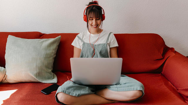 Woman with headphones working on laptop in living room 