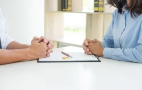 Foto que ilustra matéria sobre usucapião familiar mostra um contrato de divórcio em cima de uma mesa com duas alianças e uma caneta sobre ele. De cada lado da mesa estão um homem e uma mulher (Foto: Shutterstock)