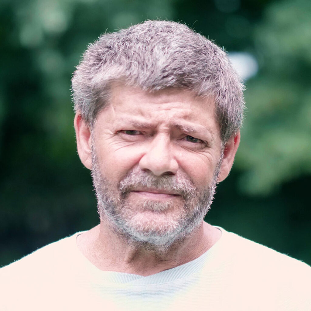 A man in a white shirt standing in a rural field.