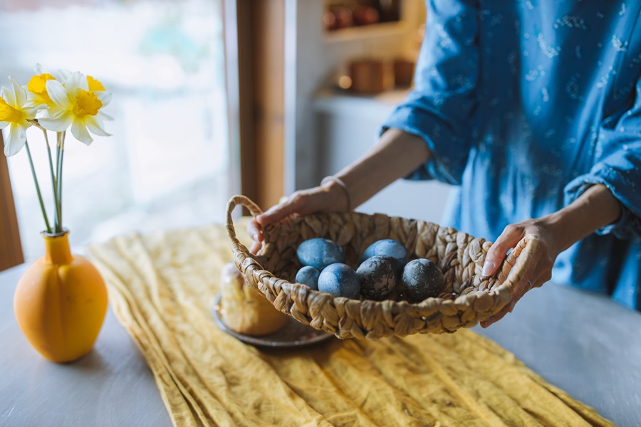 Easter Basket Ideas for Adults A Woman Putting a Basket Centerpiece Filled with Colored Eggs on a Table