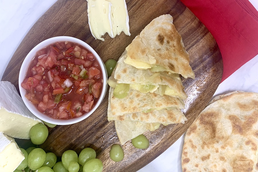 Brie and Grape Quesadilla Recipe Quesadilla Pieces on a Cutting Board with a Cup of Salsa Next to It