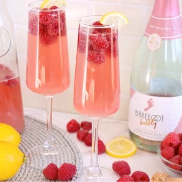 Two glasses of raspberry mimosa with raspberries and lemons.