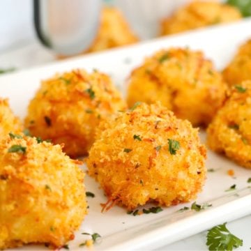 Mac and cheese filled balls on a white platter in front of an air fryer.