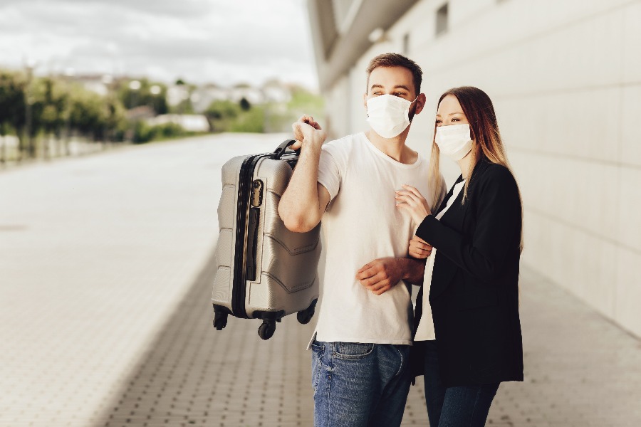 casal com malas e máscaras se preparando para viajar de ônibus durante a pandemia de coronavírus