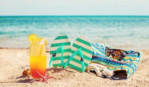 Picture of towel, flipflops, and sunglasses at the beach with gentle waves in background