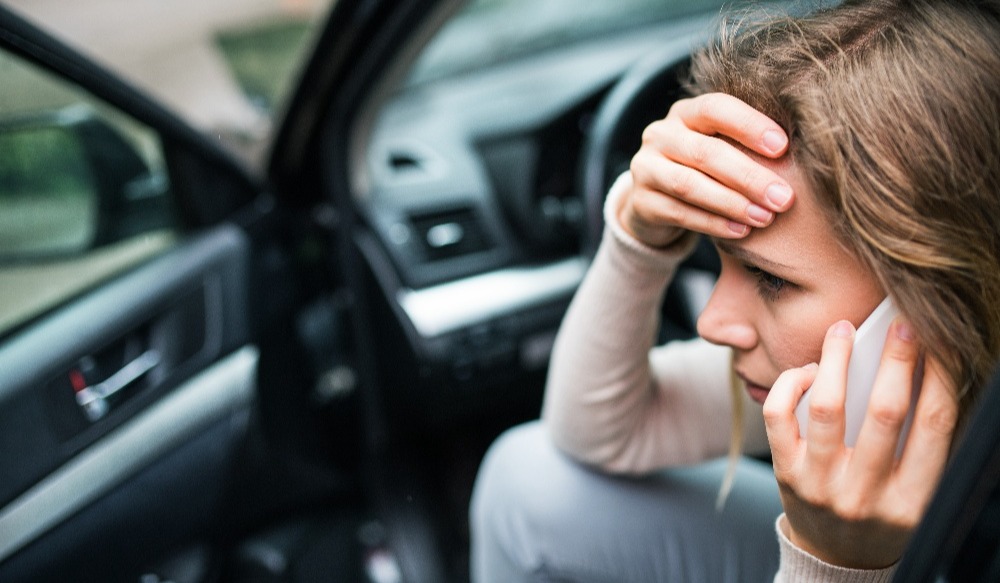 Young woman in the damaged car after a car accident, making a phone call.