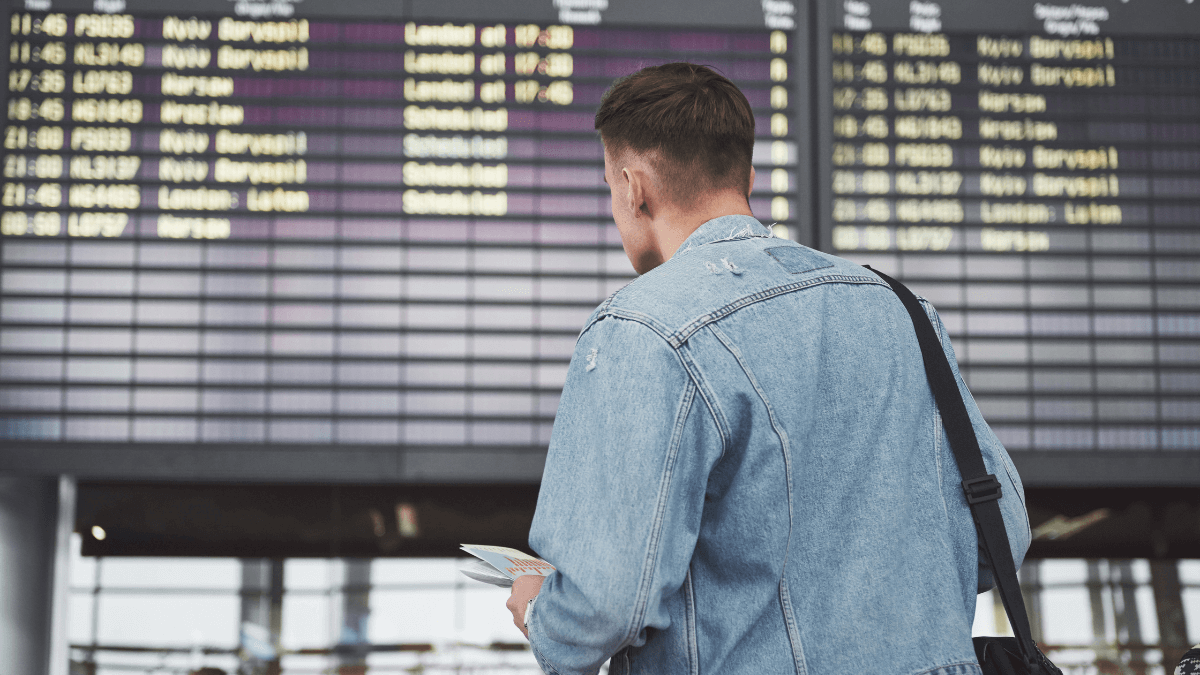 Pessoa em frente ao painel do aeroporto com passagem aérea na mão