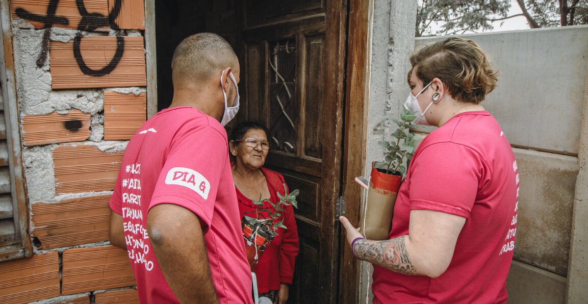 voluntários da gerando falcões conversando com uma senhora na porta de casa