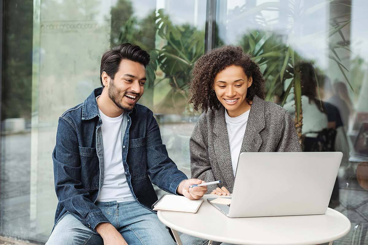 Um homem e uma mulher sentados e conversando sobre algo que está em um computador em cima da mesa.