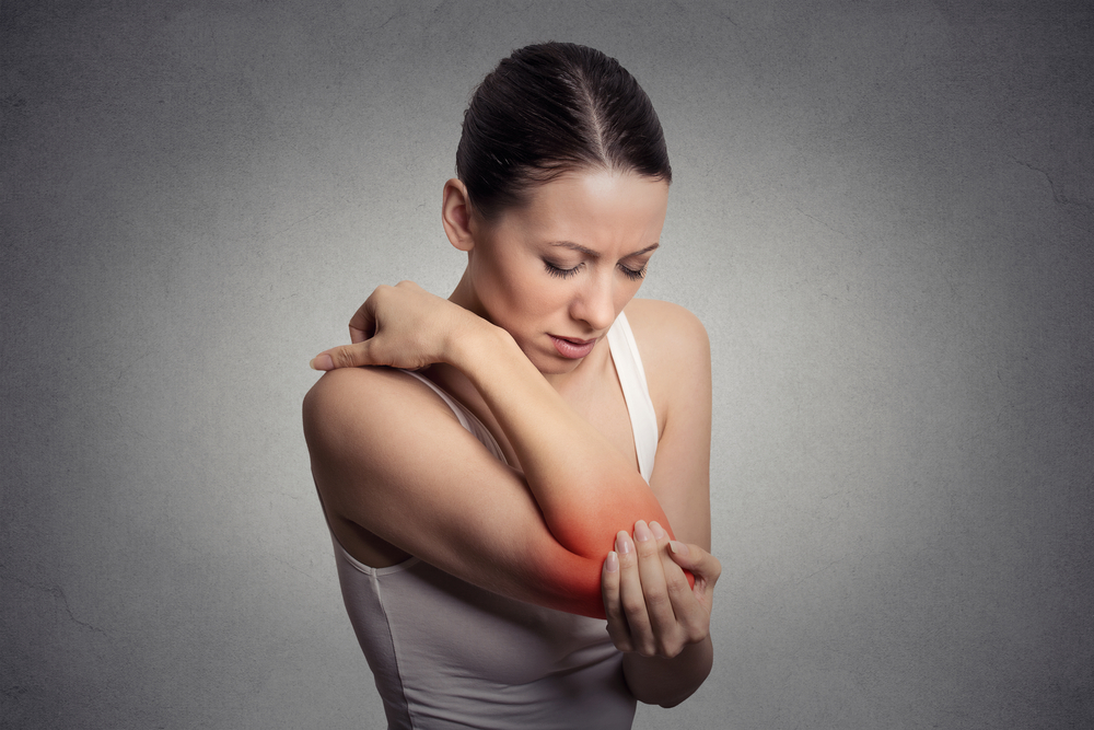 Joint inflammation indicated with red spot on female's elbow. Arm pain and injury concept. Closeup portrait woman with painful elbow on gray background