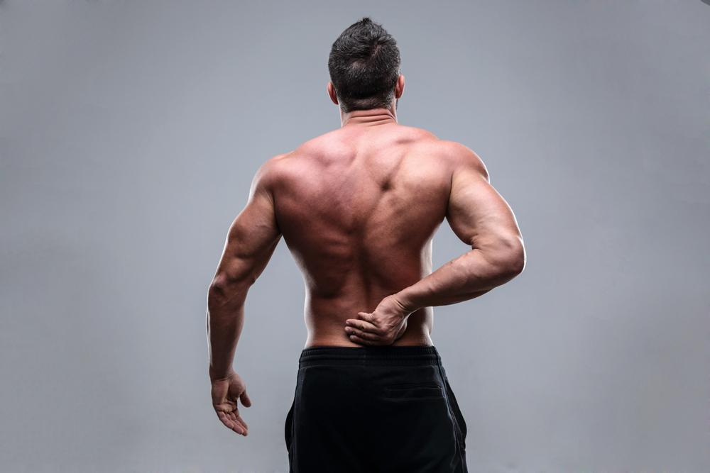 Muscular man with back pain on a gray background-1