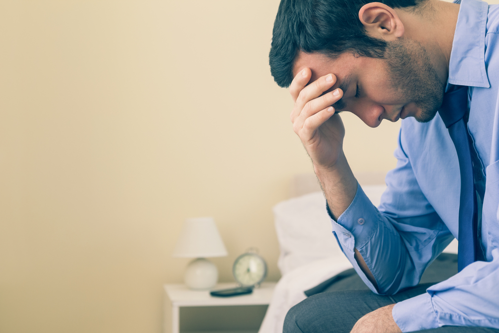 Sad man sitting head in hands on his bed in a bedroom at home-1