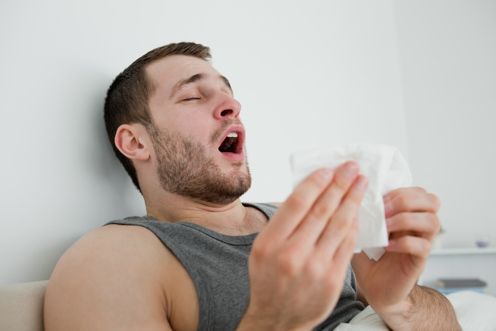 Sick man sneezing in his bedroom