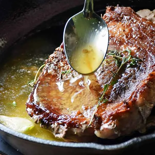 Pan seared sirloin steak in a cast iron skillet being basted with garlic-thyme butter