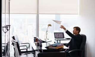 Corporate manager in modern office takes a break and prepares a paper airplane. The bored man dreams of his next vacations and l