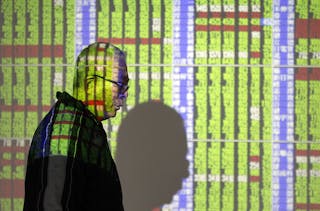 A man walks in front of monitors displaying stock market prices inside a brokerage in Taipei