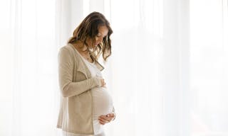 Portrait of young pregnant attractive woman, standing by the window, dressed in white dress, isolated image - 圖片