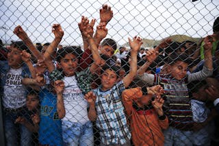 Refugee youths gesture from behind a fence as officals arrive at Nizip refugee camp near Gaziantep