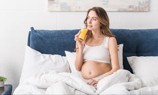 Dreamy pregnant woman drinking juice in bed — Photo by AndrewLozovyi