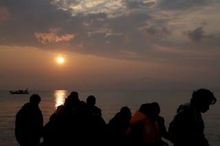 Refugees are silhouetted as they reach the shores of the Greek island of Lesbos on a dinghy during sunrise