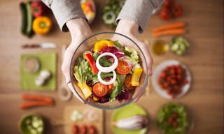 Hands holding an healthy fresh vegetarian salad in a bowl, fresh raw vegetables on background, top view