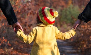 Young Family Walking on Park Alley Parents Holding Hands of Little Baby Daughter from both Sides Autumnal Colorful Forest on Bac