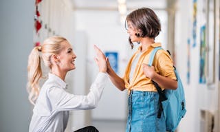 Teacher giving high five to adorable schoolgirl in school corridor — Photo by ArturVerkhovetskiy