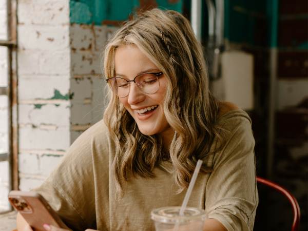 woman sits in a cafe drinking coffee while smiling at her phone, illustrating increasing Instagram reach