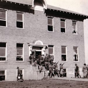 Group of soldiers in uniform on steps of multistory brick building