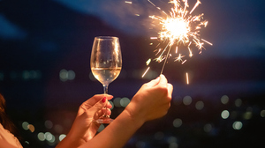 A young woman&rsquo;s hand holds a glass of champagne and a sparkler.