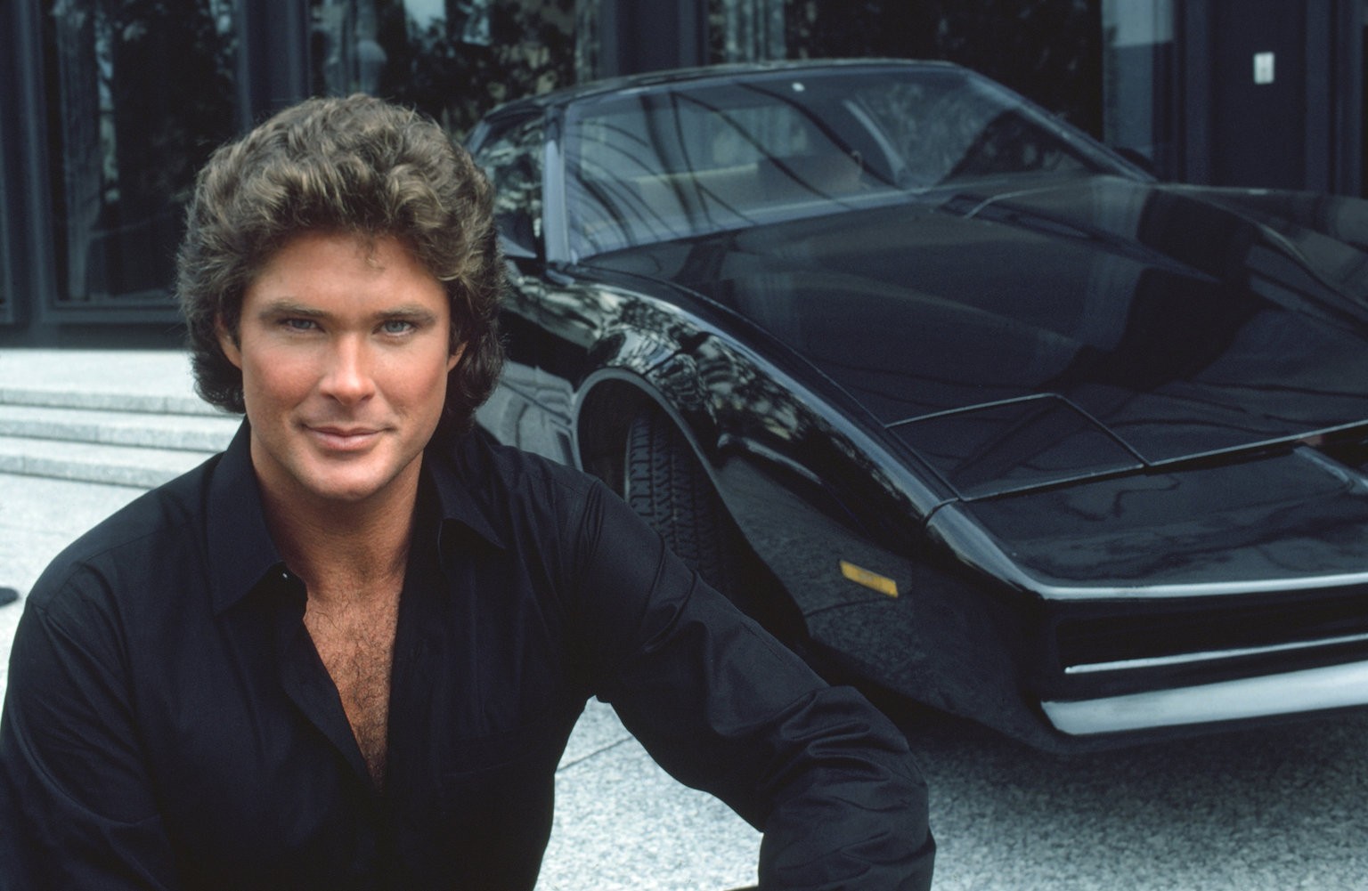 män, ansikte, bil, byggnad, ser tittaren, utomhus, fordon, skådespelare, leende, skjorta, fordonets främre, 1980, svarta bilar, sportbil, Pontiac, TV-serier, David Hasselhoff, K I T T, Michael Knight, Knight Rider, legend, körning, superbil, landfordon, bildesign, bil make, lyx fordon