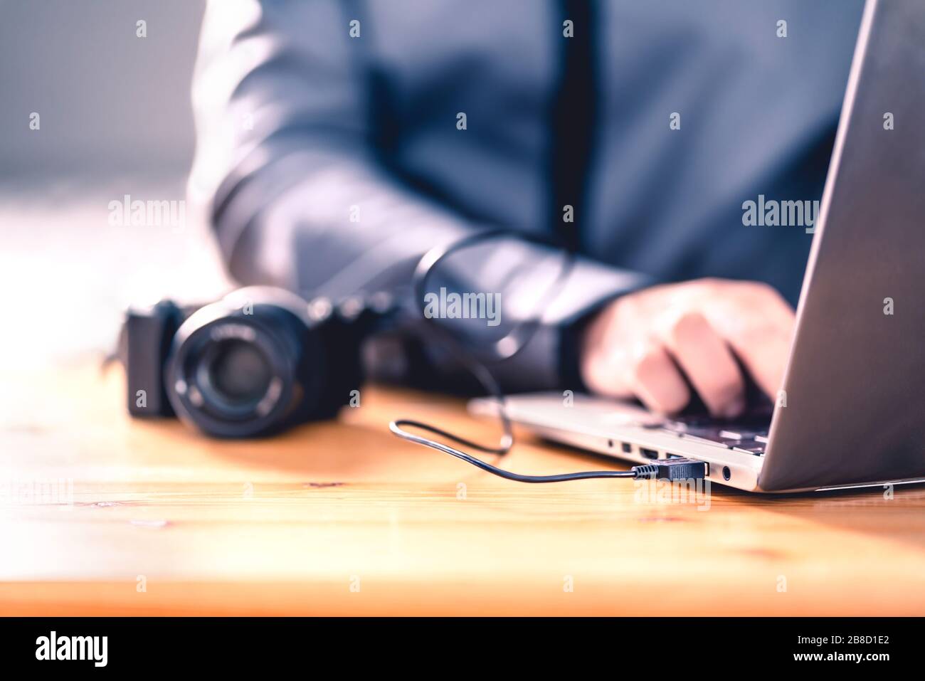 Camera connected to laptop with usb cable. Man editing photos with computer software. Photographer transfer files to computer from DSLR. Stock Photo