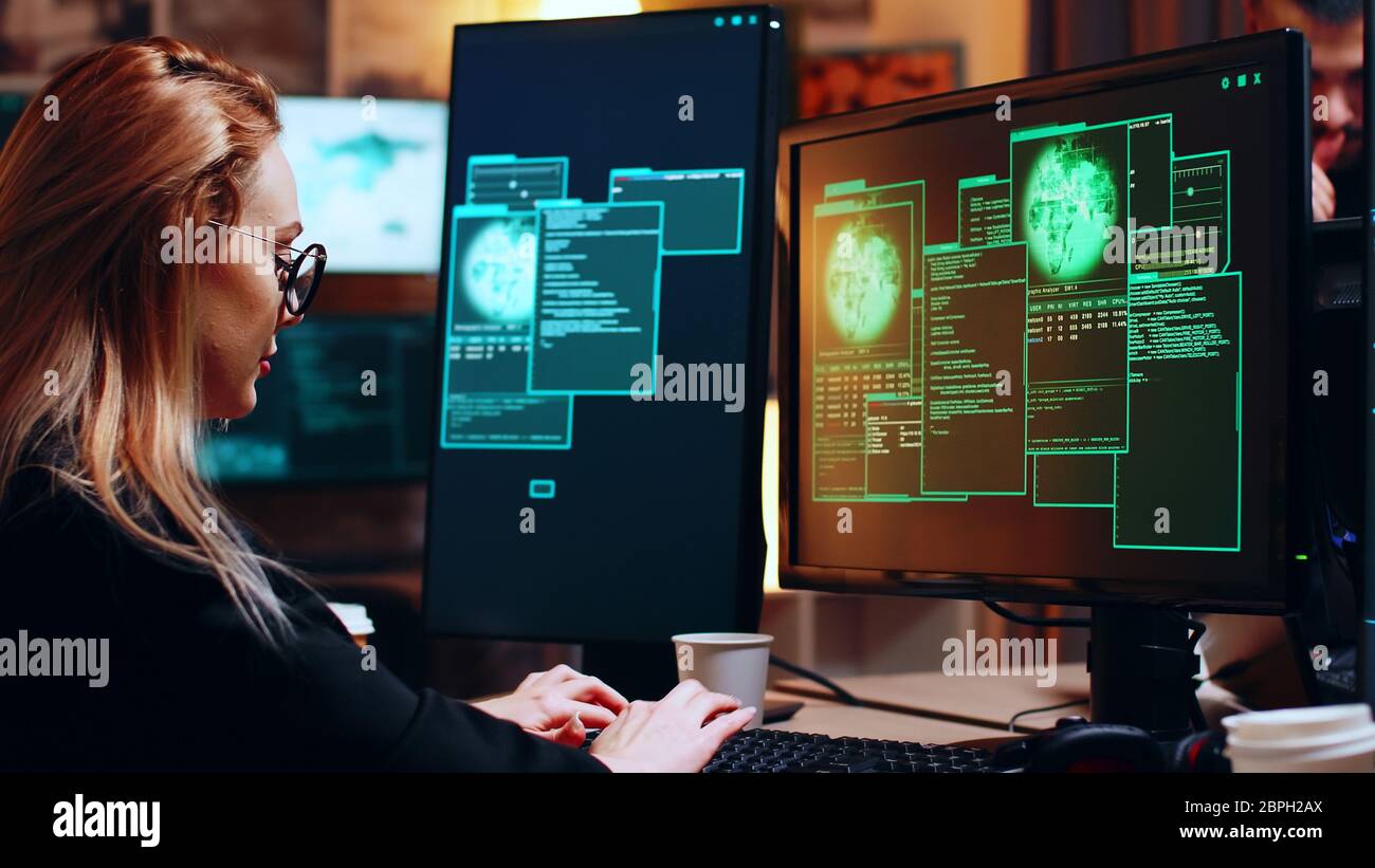 Girl hacker looking at super computer with multiple monitors while writing a malware. Stock Photo