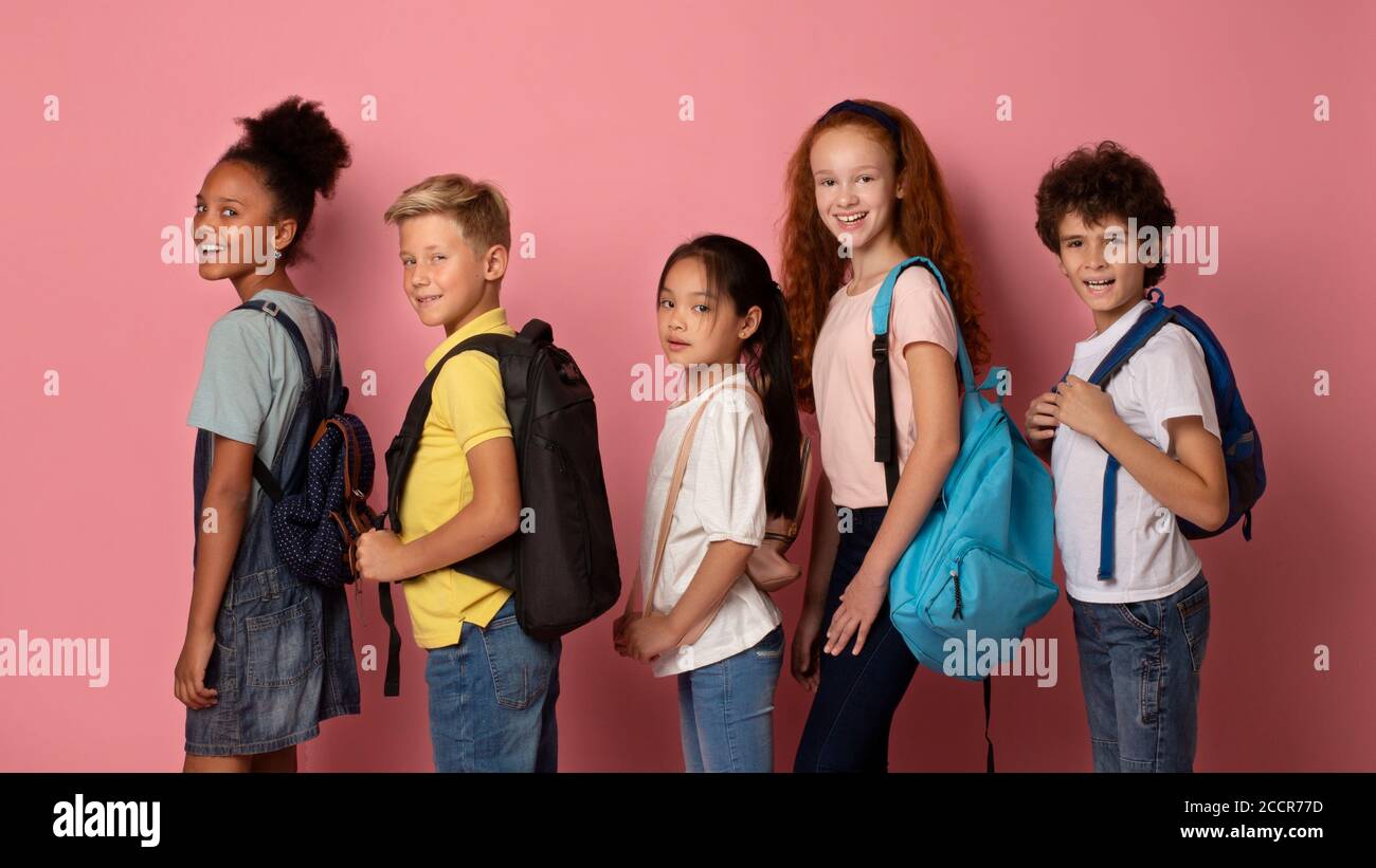 Joyful kids with backpacks going to school one after another on pink background Stock Photo