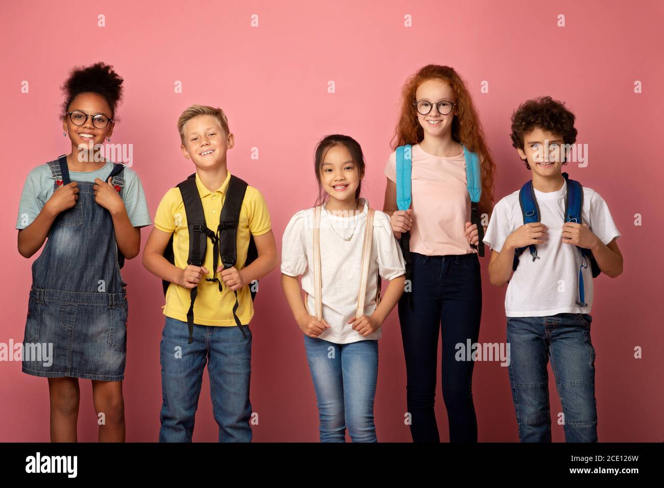 Back to school. Joyful children with backpacks standing together on pink background Stock Photo